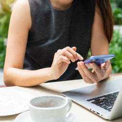 remote worker sits outdoors with a smartphone and laptop computer