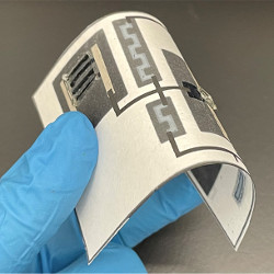 gloved fingers hold bendable paper-based electronics