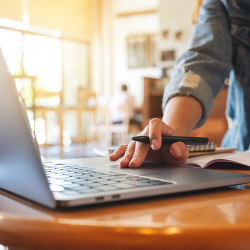 person writing in a notebook and on a laptop computer