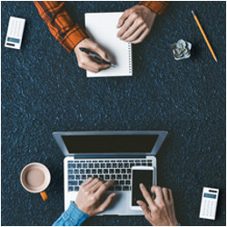 casually dressed men, one writing and another on a laptop computer, seen from above