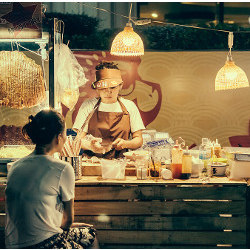 woman sitting at an Asian food stand