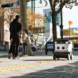 An autonomous robot shares the sidewalk with pedestrians. 