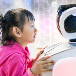 a young girl looks at and leans into the face of a robot