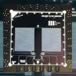 A backside-illuminated optical photograph of a fabricated device with false coloring, showing all components including the 2 mlong coplanar waveguide, as well as the printed circuit board to which the die is wirebonded for signal routing.